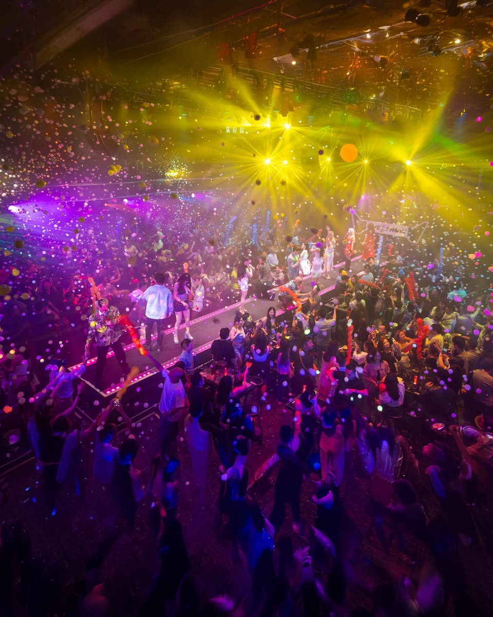 People enjoying an outdoor performance or event, illuminated by festive lights.