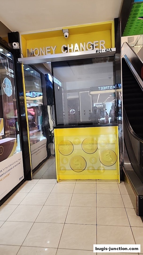 The exterior of a bright yellow money changer booth with signage and security cameras.