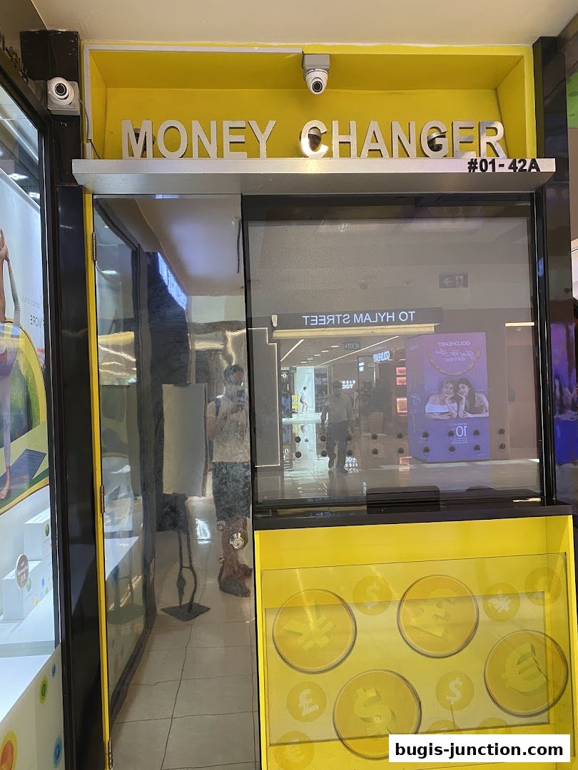 Exterior of a bright yellow money changer shop with prominent signage and currency symbols.