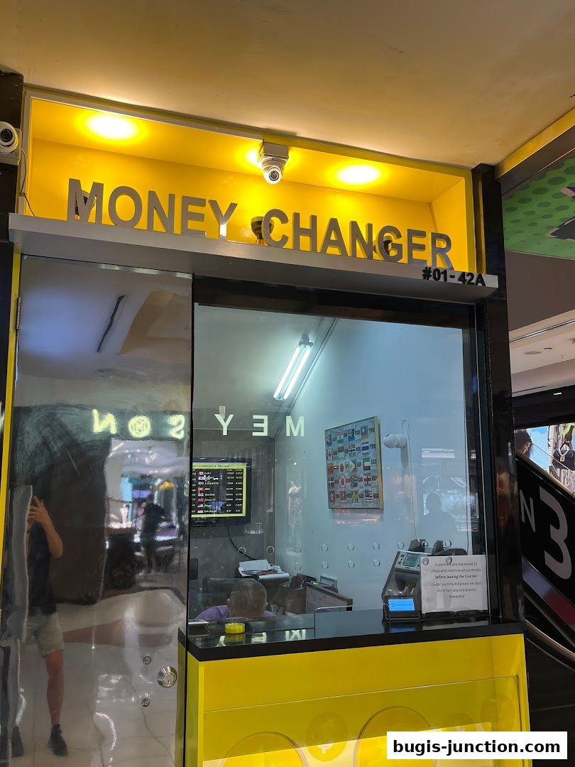Exterior of a brightly lit money changer shop with prominent signage and a display of currency exchange rates.