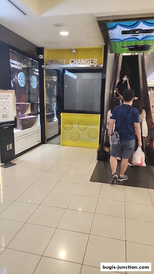 The exterior of a money changer shop with a yellow sign and a display of coins.