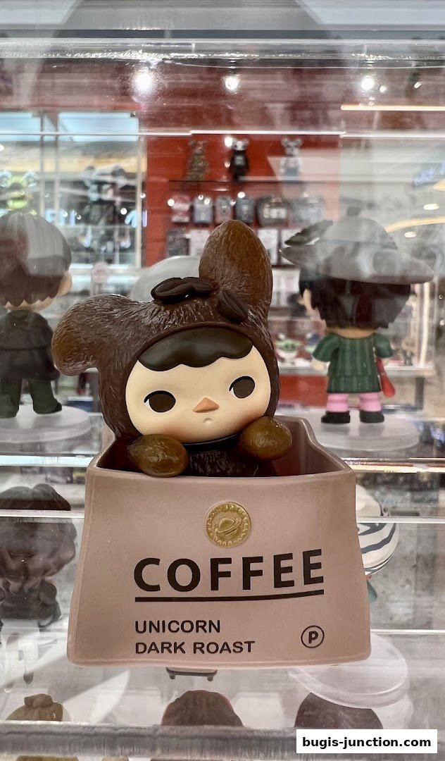 A cute collectible toy with a coffee theme is displayed in a shop window.