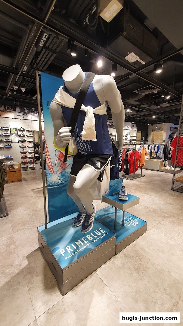 Mannequin dressed in Adidas athletic wear, showcasing Primeblue collection, with shoes and apparel displayed.