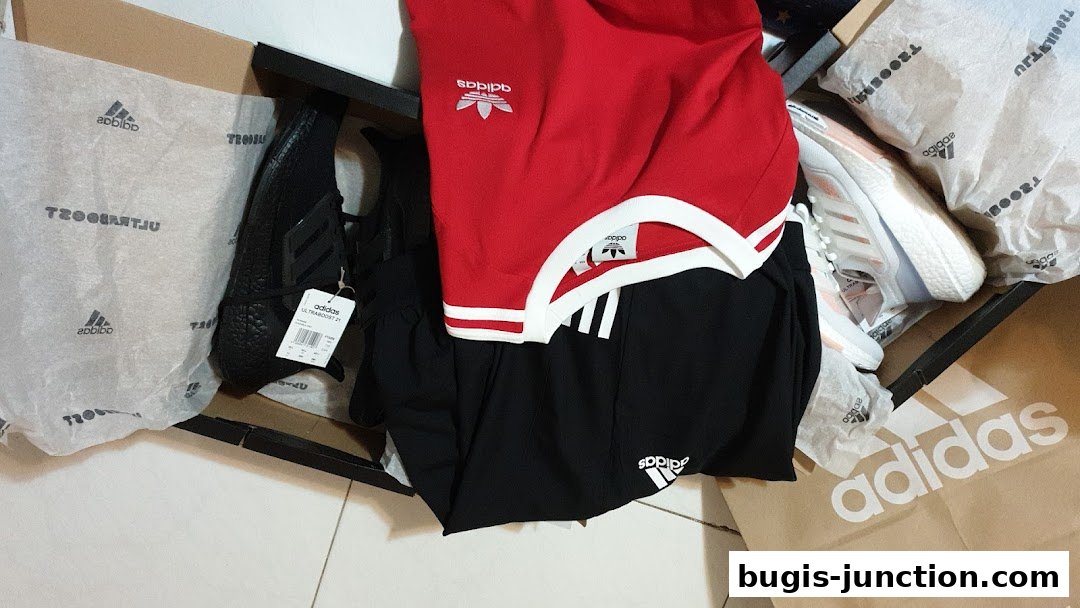 Adidas apparel and shoes are displayed in boxes and shopping bags.