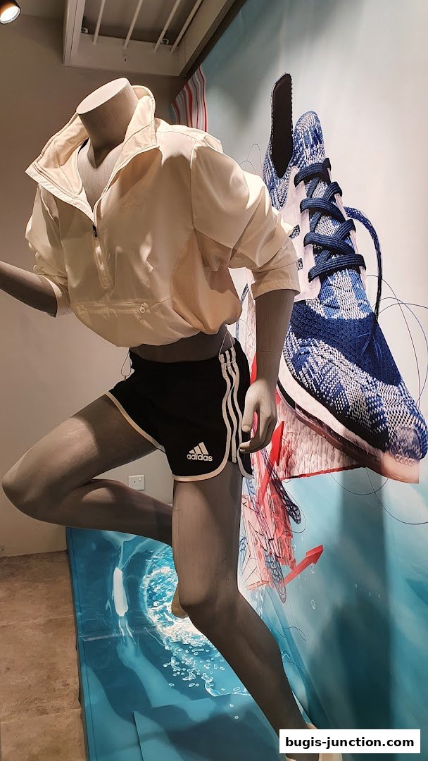 Mannequin wearing Adidas athletic wear with a large shoe graphic in the background.