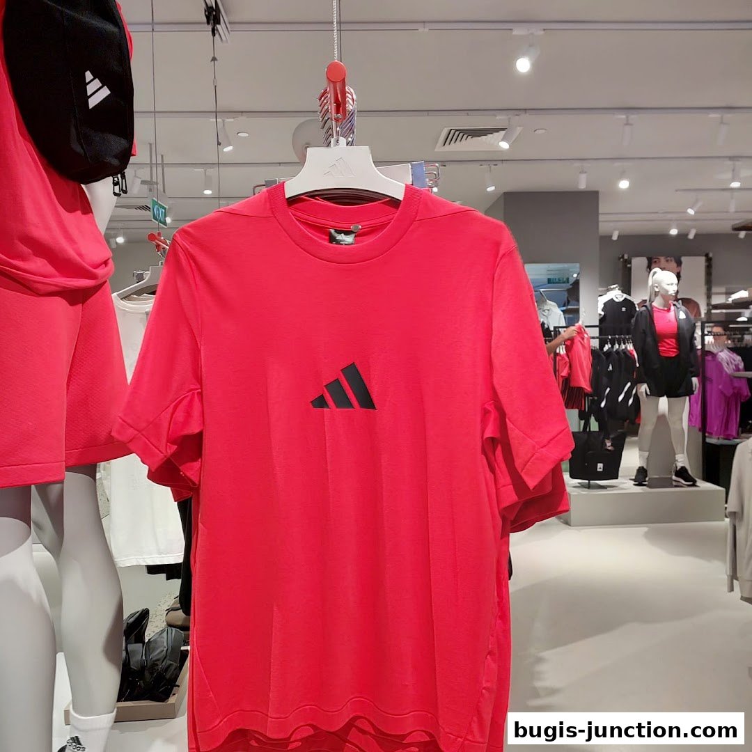 A bright red Adidas t-shirt with a black logo displayed on a hanger in a store.