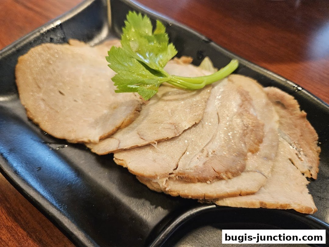 Thinly sliced roasted pork with a sprig of parsley on a black plate.