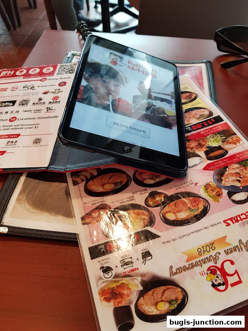 A table with menus and a tablet displaying the Ajisen Ramen ordering interface.