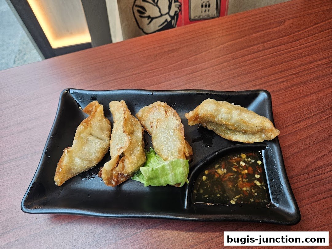 A plate of golden-brown pan-fried dumplings served with dipping sauce and lettuce.