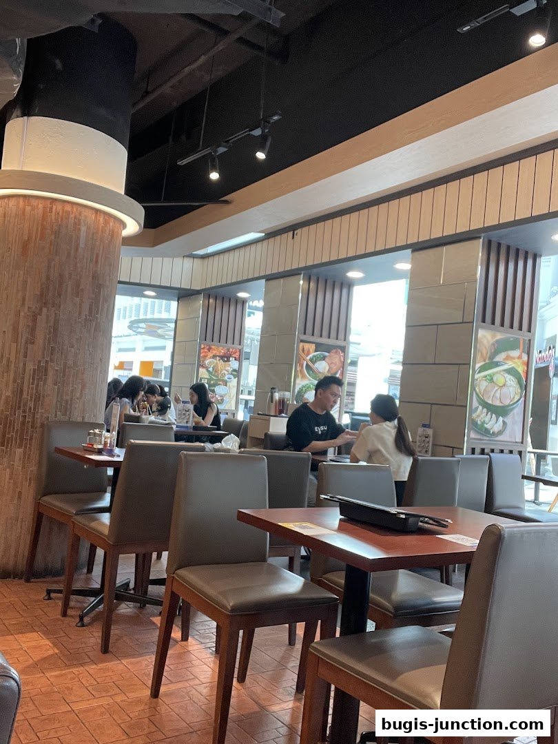 Interior view of Ajisen Ramen with diners seated at tables and ramen posters on the wall.