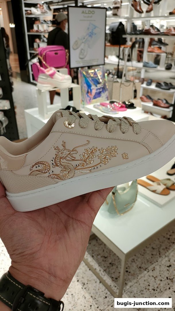 A hand holds a stylish beige sneaker with a dragon and floral design.
