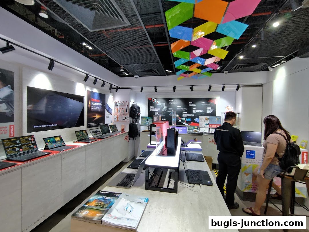 Interior of a Lenovo store showcasing laptops and tech accessories with customers browsing.