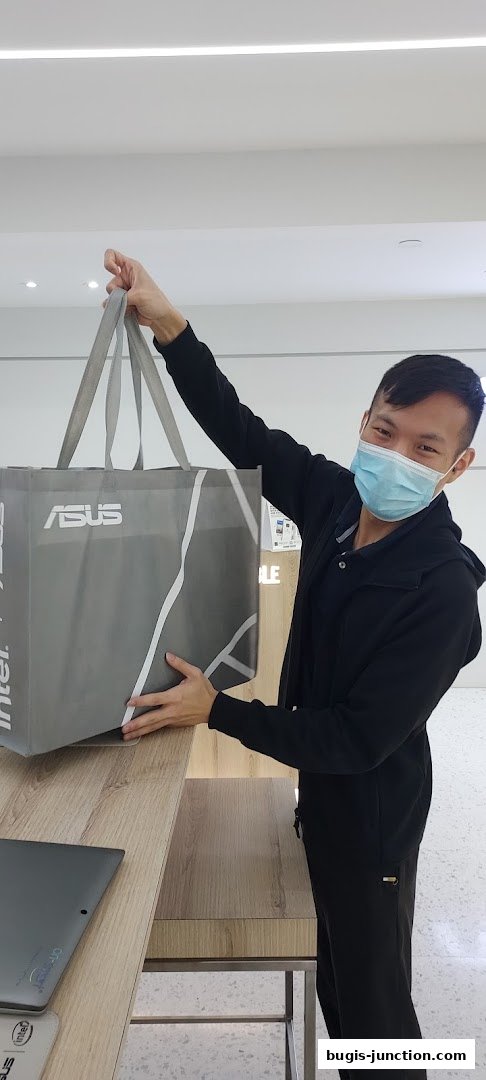 A smiling man wearing a mask holds an ASUS shopping bag inside a store.