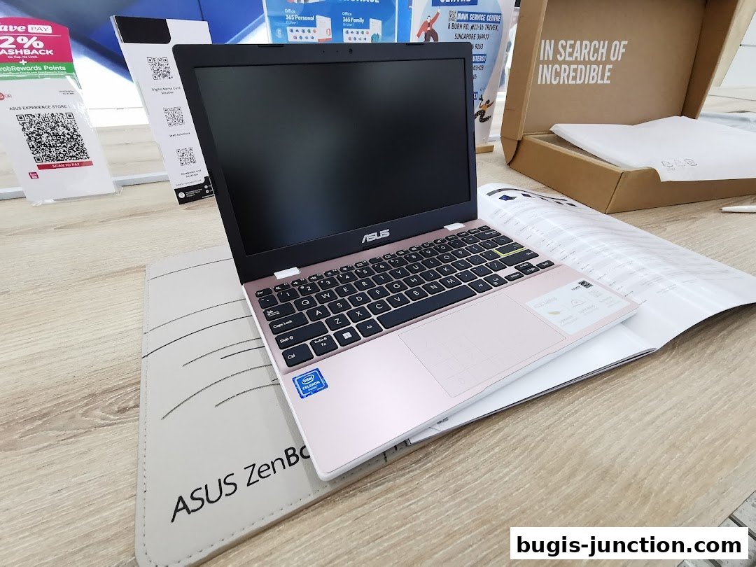 A pink ASUS ZenBook laptop is displayed on a wooden surface with promotional materials.
