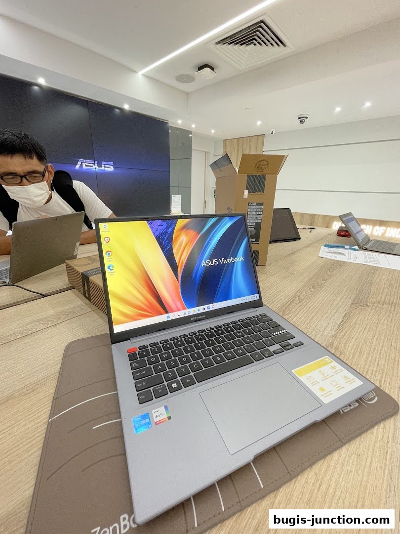 An ASUS Vivobook laptop is displayed on a wooden table in a modern electronics store.