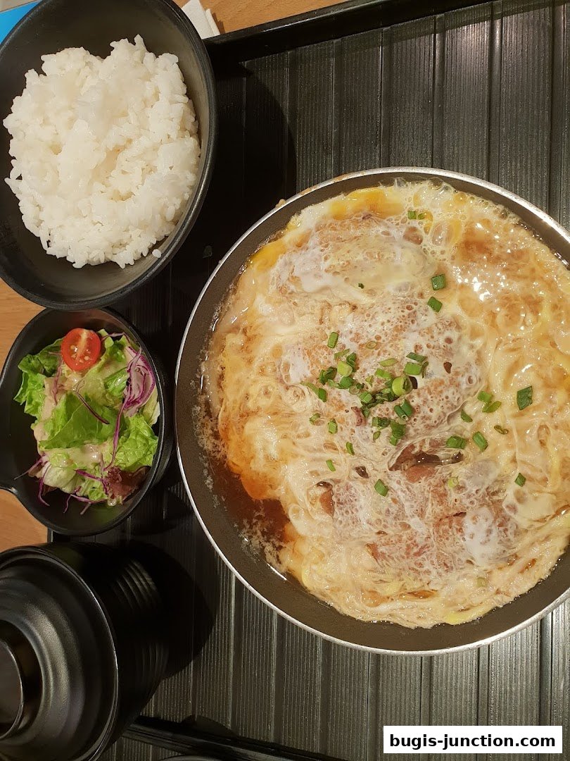 A Japanese Oyakodon dish with rice and a side salad on a tray.