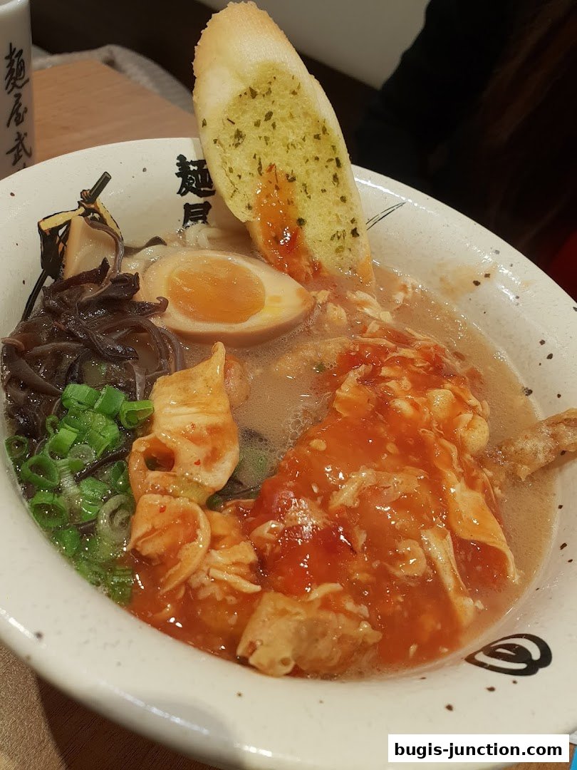 A close-up of a bowl of ramen with a slice of garlic bread on top.