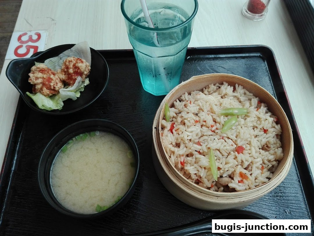 A Japanese meal set featuring fried chicken, miso soup, fried rice, and a drink.
