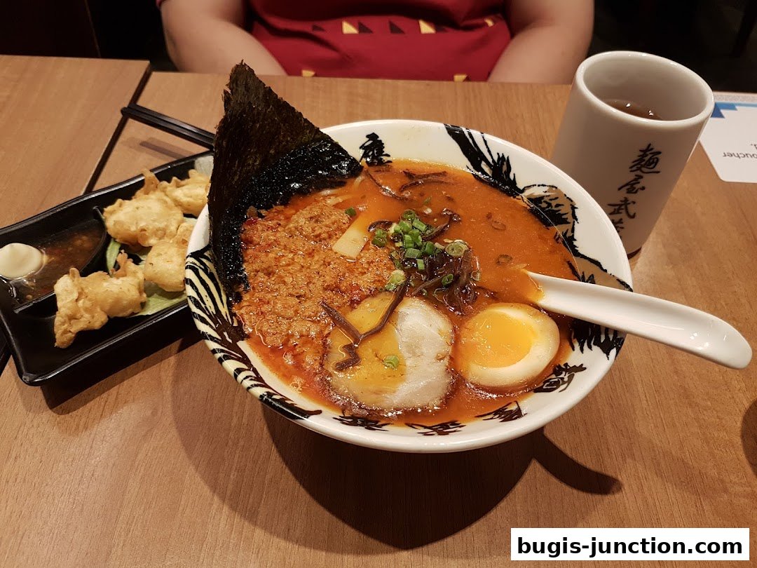 A bowl of ramen with a side of fried appetizers and a cup of tea.