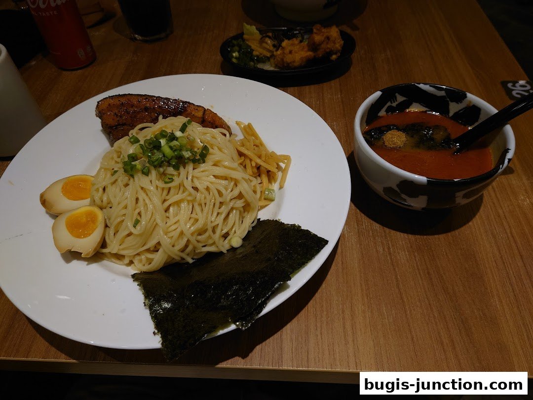 A plate of ramen with chashu pork, soft-boiled eggs, and nori, served with a side of dipping broth.