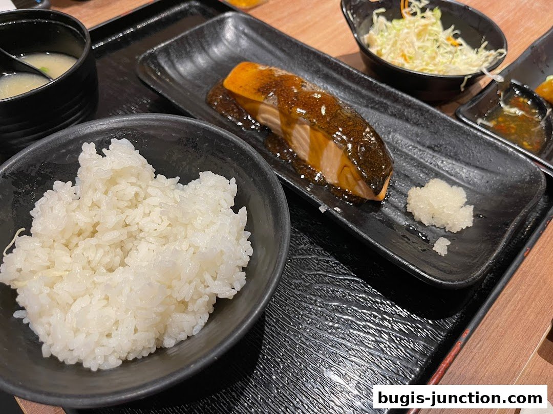 A close-up of a Japanese meal featuring grilled salmon, rice, miso soup, and salad.