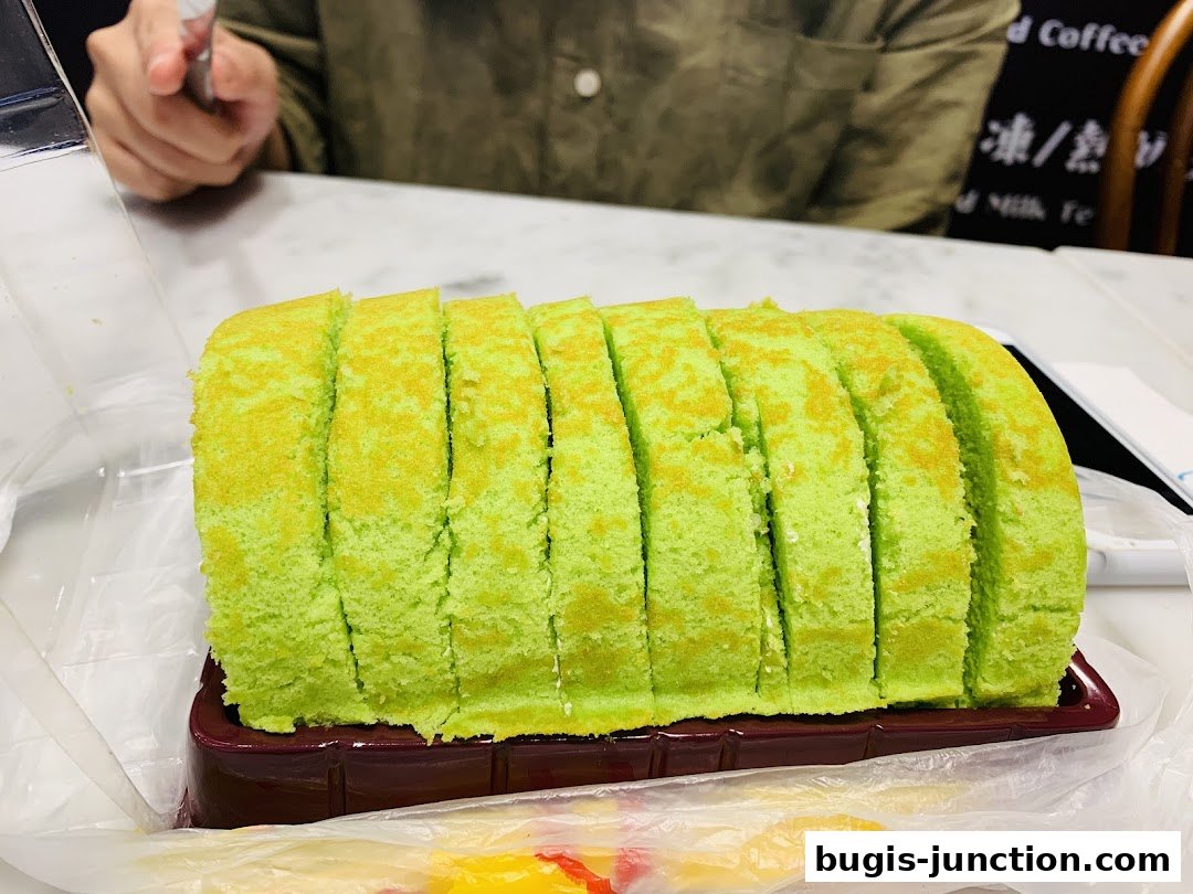 A sliced green pandan swiss roll cake in a plastic container, ready to be enjoyed.