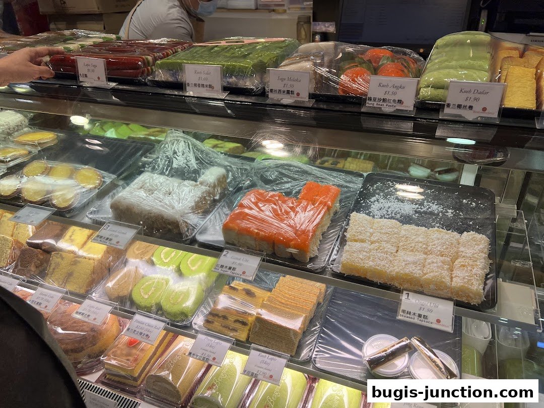 A display case filled with various colorful cakes and pastries, neatly packaged and labeled.
