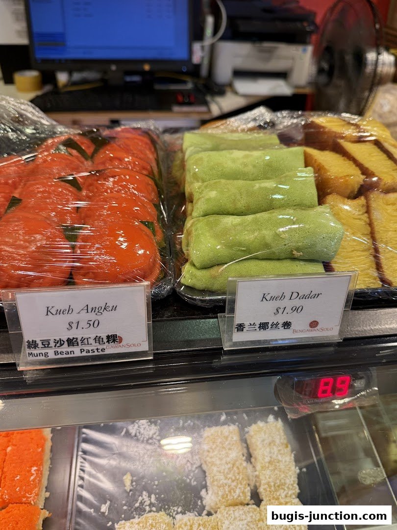 A display of colorful Southeast Asian desserts, including Kueh Angku and Kueh Dadar.
