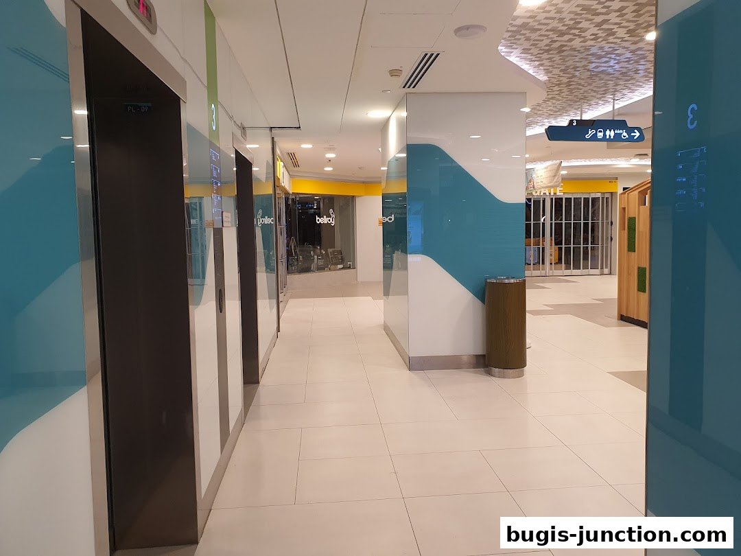 A modern shopping mall corridor with elevators and shop entrances.