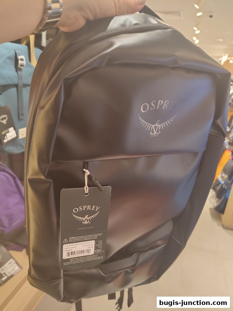 A person holds a black Osprey backpack with a tag attached.