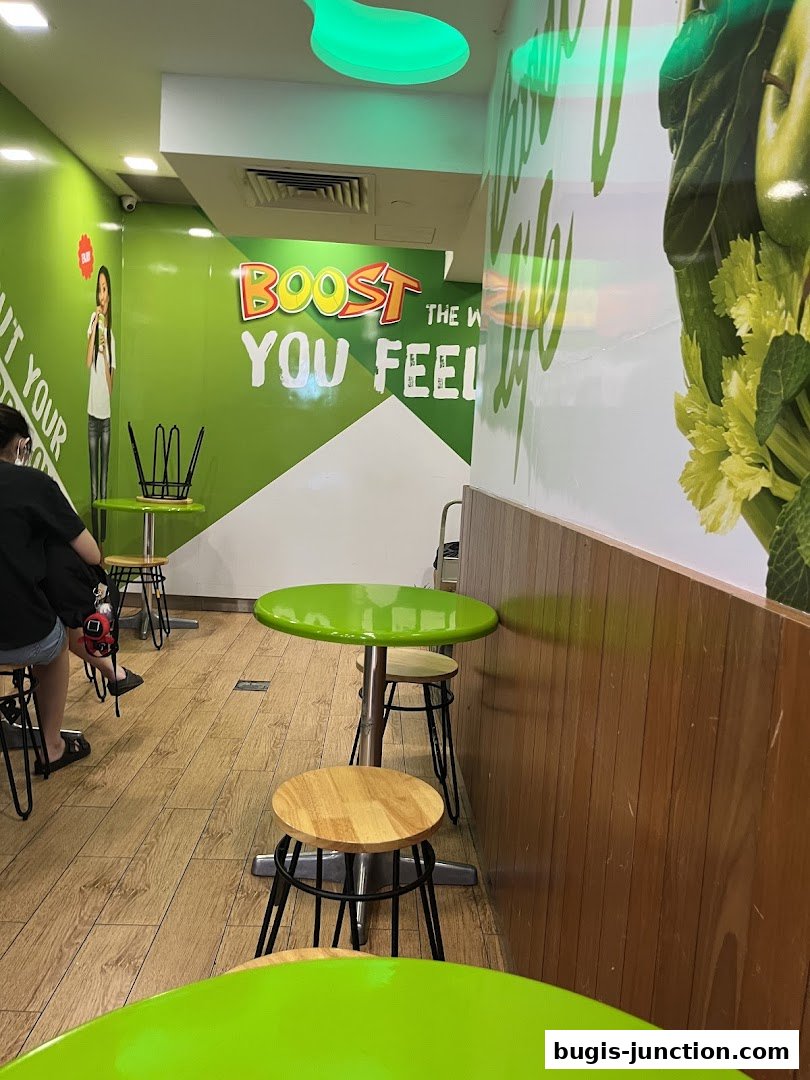 Interior of a Boost Juice shop with green tables and stools, and branding on the wall.