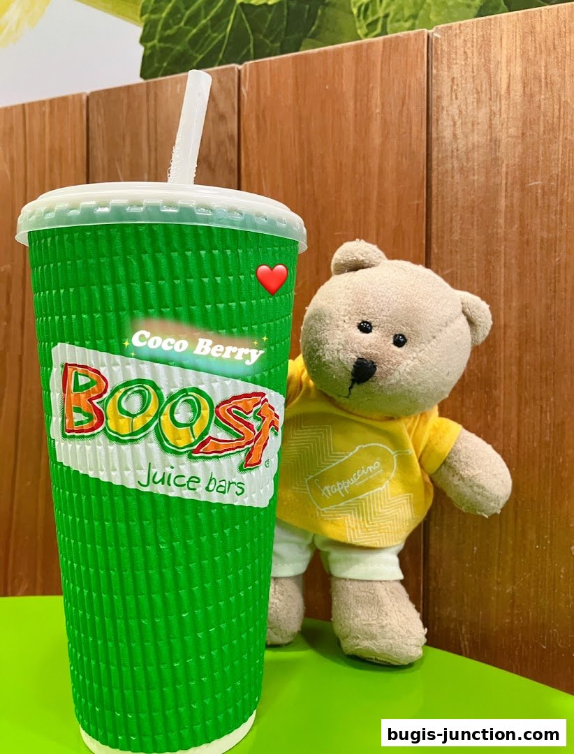 A green Boost Juice cup with a teddy bear wearing a yellow shirt.