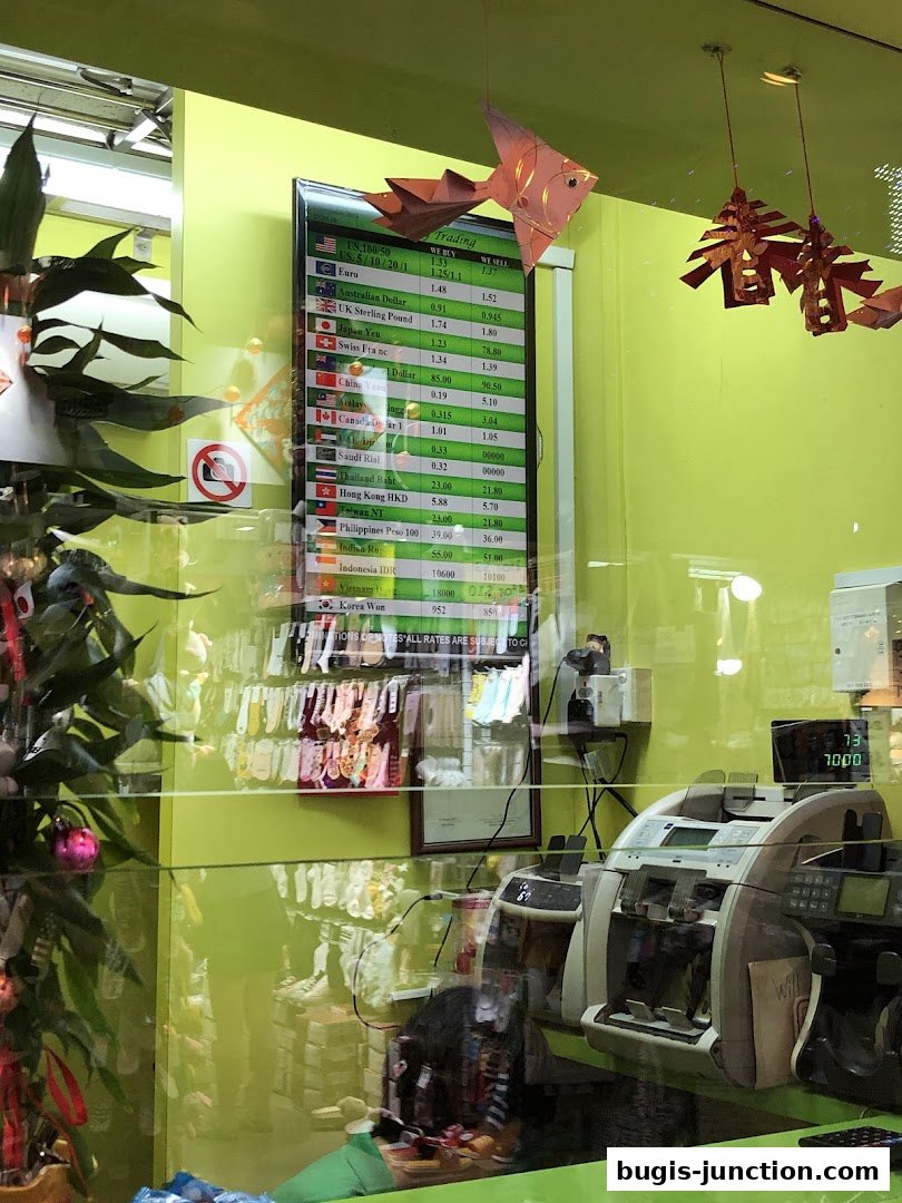 A money changer shop with a currency exchange rate board and money counting machines.