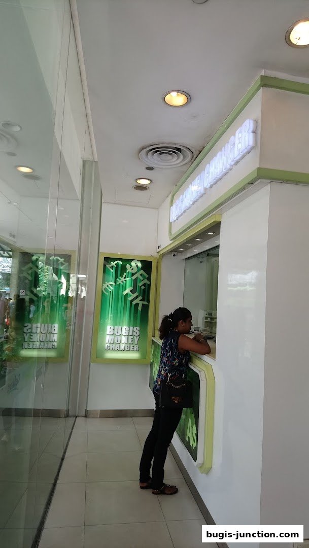 A woman stands at the counter of Bugis Money Changer, a currency exchange service.