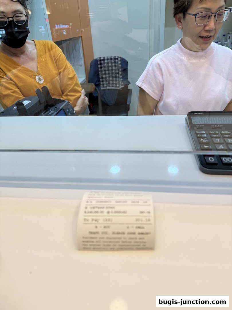 Two women are seen behind a counter at a money changer, with a receipt visible.
