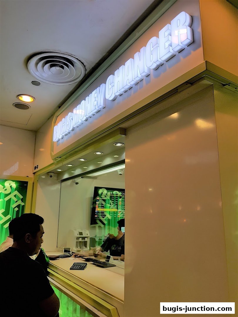 Bugis Money Changer shop front with illuminated signage and staff serving customers.
