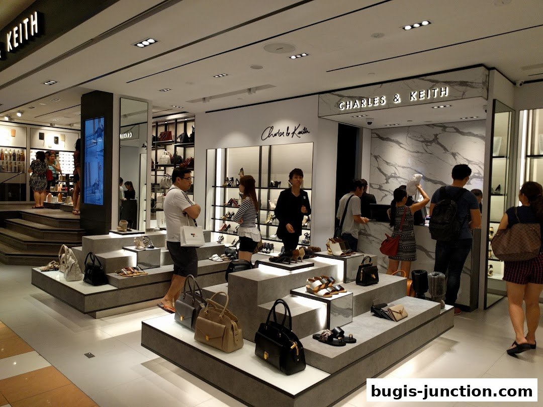 Customers browse stylish handbags and shoes displayed on tiered platforms inside a Charles & Keith store.