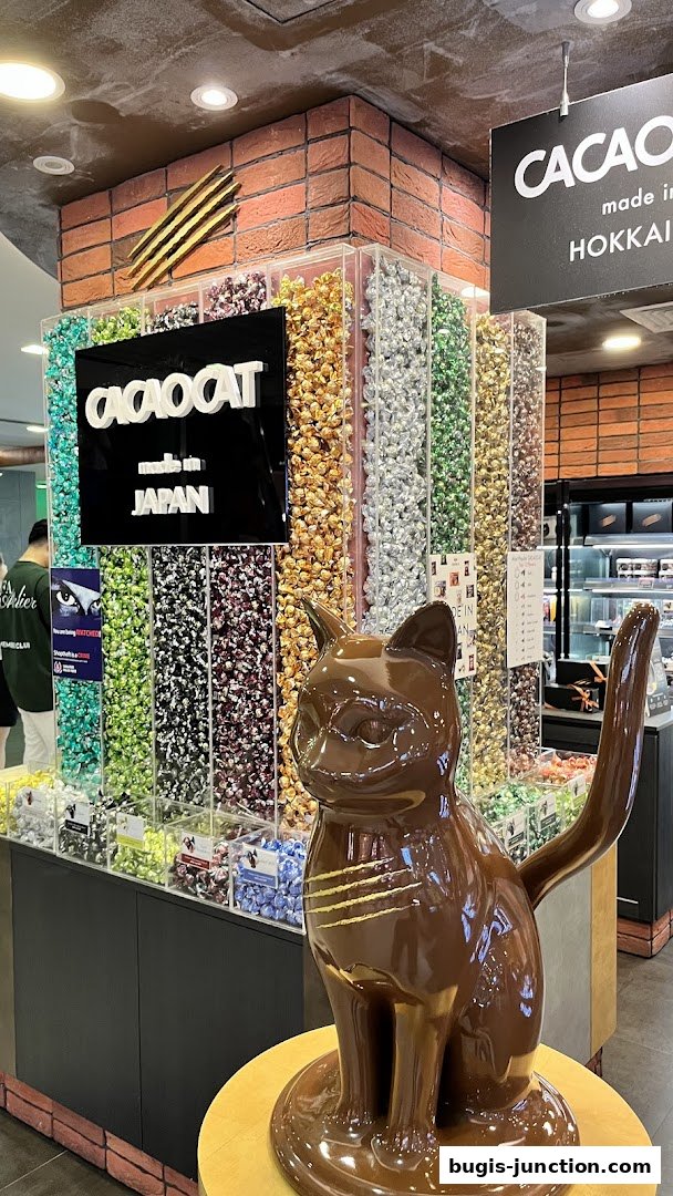 A chocolate cat statue stands in front of colorful chocolate displays at Chocolate Origin.