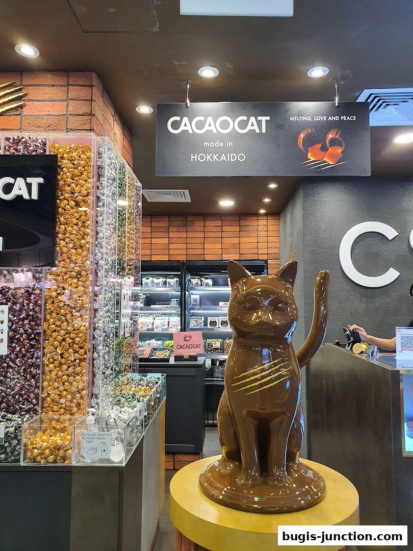 A chocolate cat statue stands in front of a display of colorful candies at Cacao Cat.