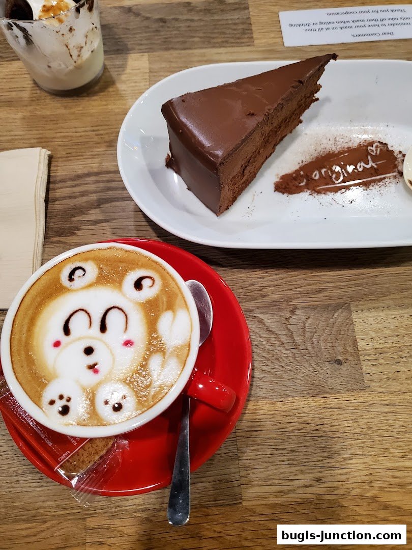 A slice of chocolate cake and a latte with bear art on a wooden table.