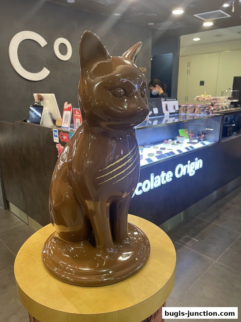 A large chocolate cat sculpture is displayed in front of the Chocolate Origin store.