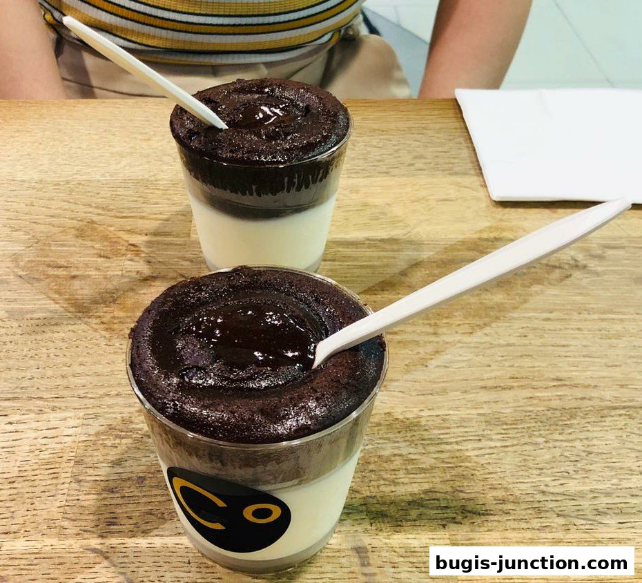 Two chocolate desserts in clear cups with spoons on a wooden table.