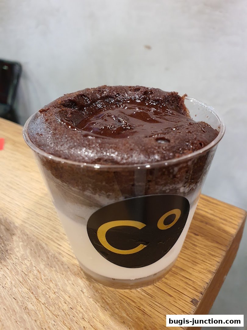 A close-up of a chocolate lava cake in a clear cup with a creamy layer.
