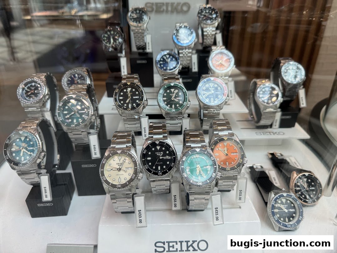 A display of various Seiko watches with metal bands and different colored faces.