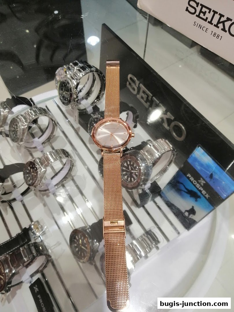 A display of various watches, with a rose gold mesh watch prominently featured.