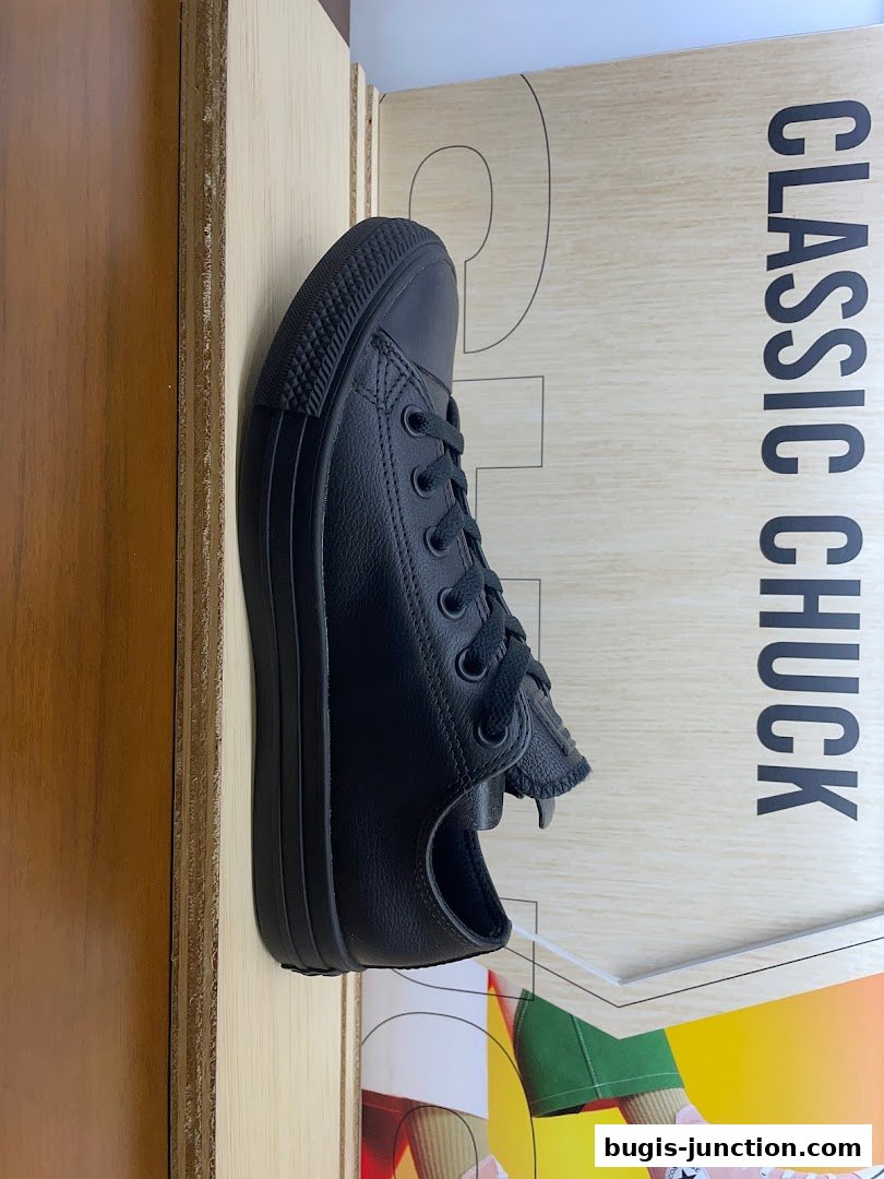 A black leather Converse sneaker displayed on a wooden surface with text.