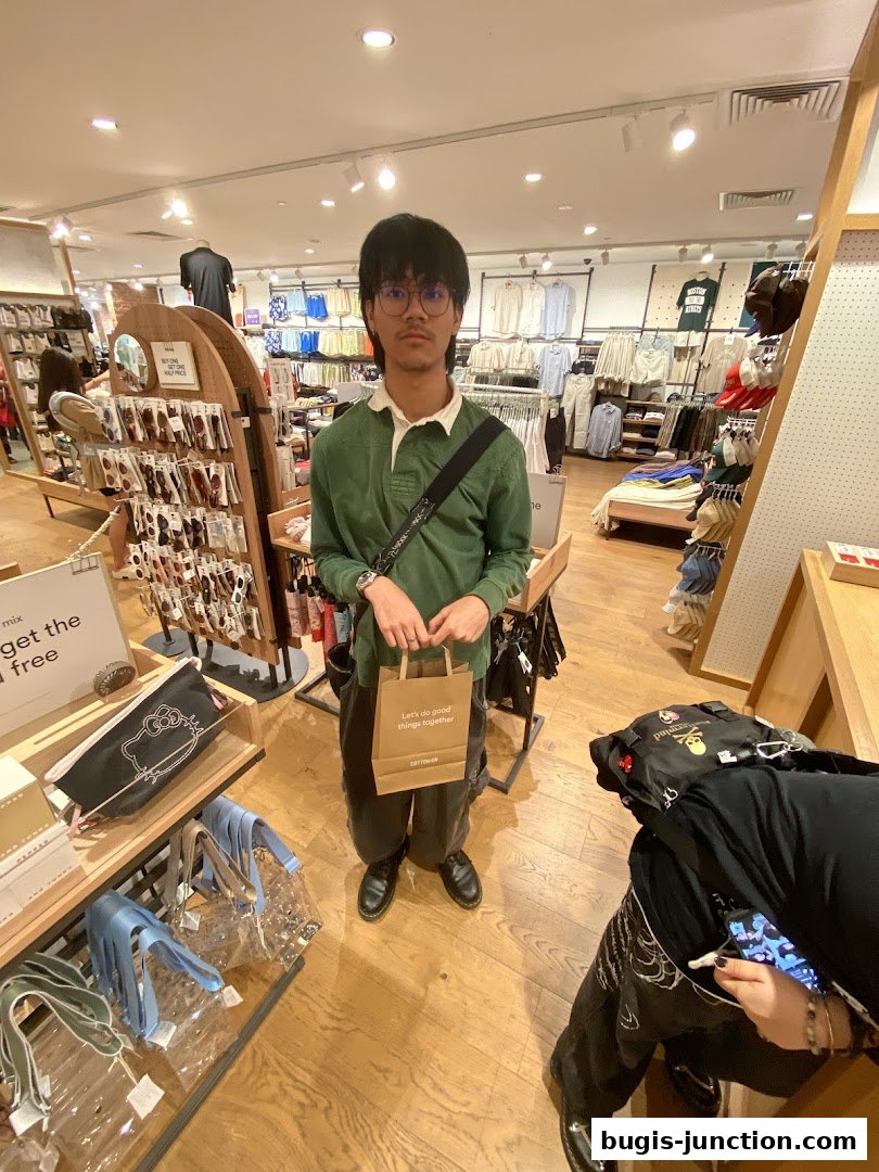 A person stands in a brightly lit clothing store, holding a shopping bag.