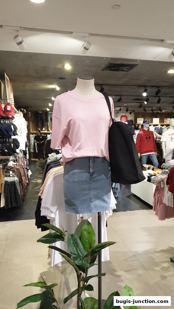 Mannequin wearing a pink t-shirt and denim skirt with a black tote bag in a clothing store.
