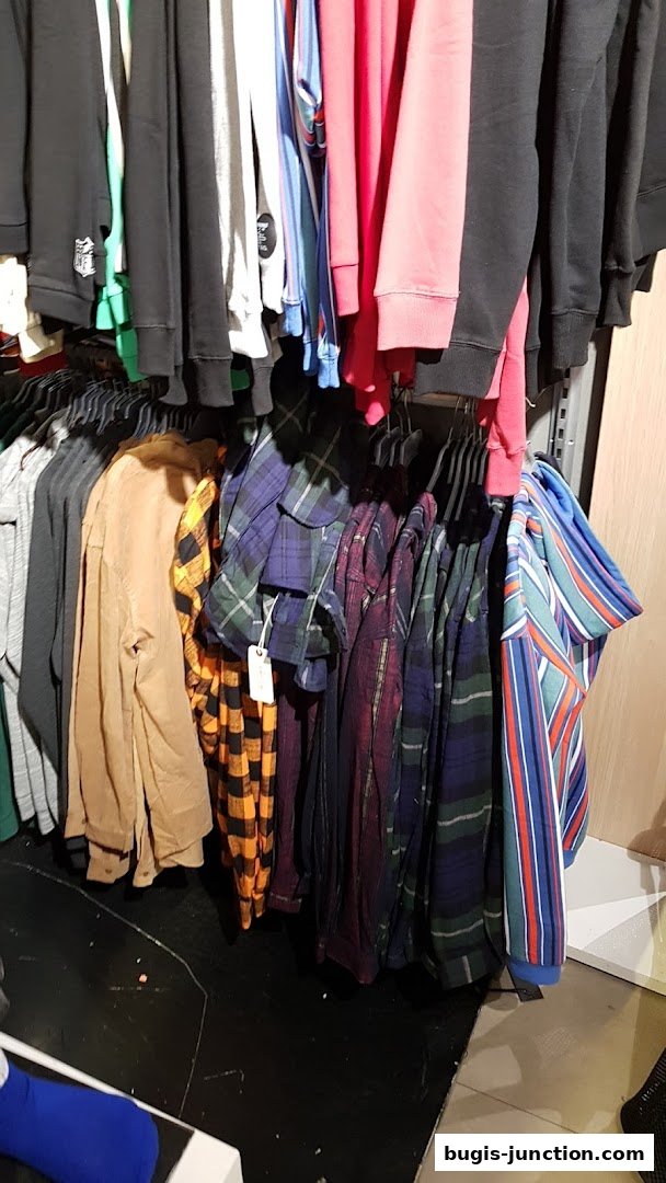 A rack of colorful plaid shirts and hoodies displayed in a retail store.