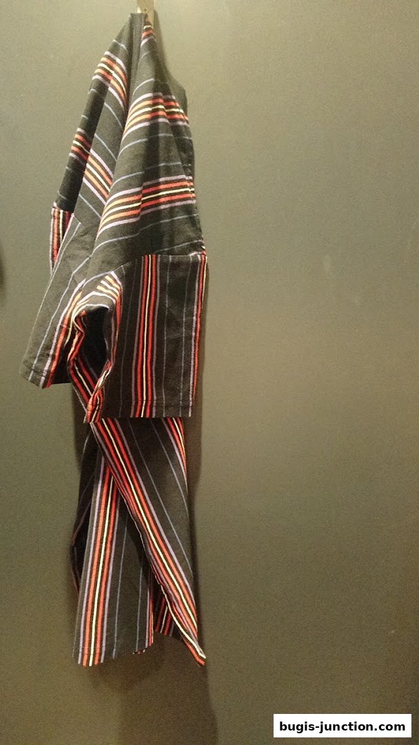 A striped garment hangs from a hook against a plain wall.